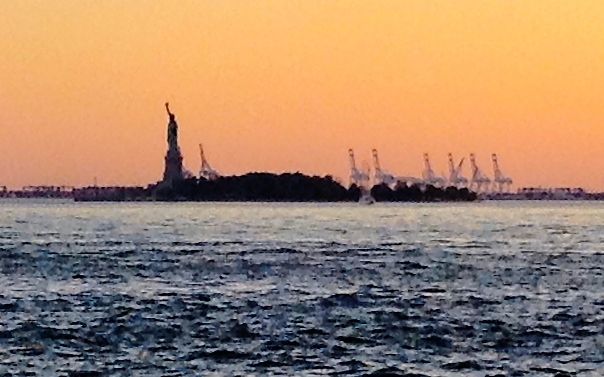 The Statue of Liberty at sunset flanked by construction cranes reminds us that the monument is a symbol of our historical role as refuge for immigrants and chief exporter of freedom. w